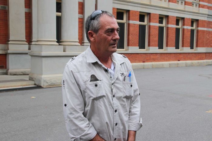 A middle-aged man with sunglasses on his head wearing a work uniform stands outside WA Supreme Court looking to one side. 